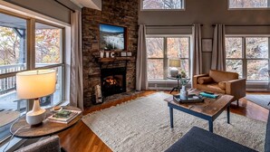 Ein gemütliches Wohnzimmer mit Kamin, großen Fenstern, einem Ledersofa und einem Holztisch.