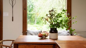 A wooden dining table with a bowl of fruit, a potted plant, and a wall-mounted light fixture. - Hudson Pond · Garden Queen Suite · GF Breakfast (Poughkeepsie)