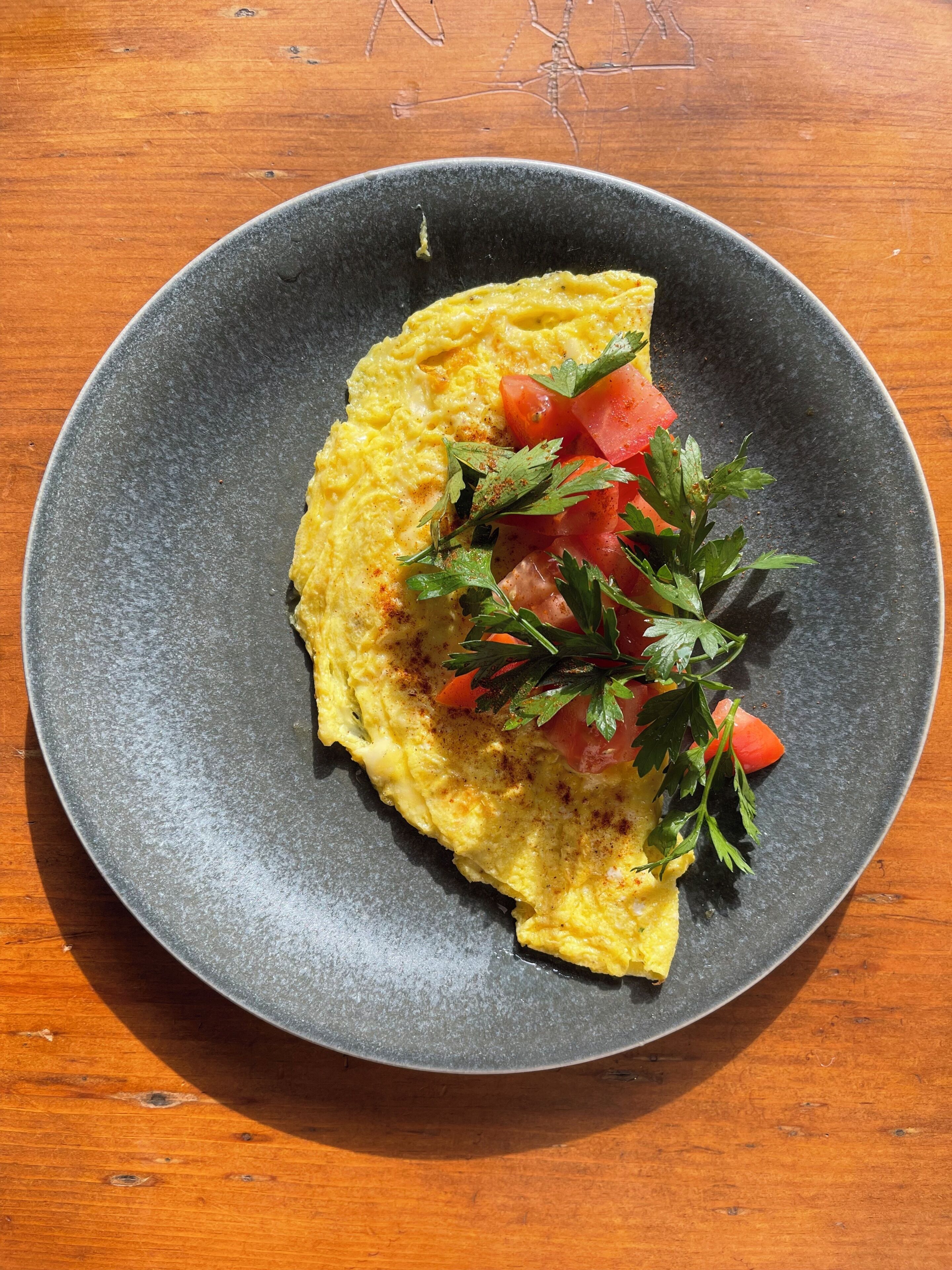 A plate with an omelette, tomatoes, and parsley on a wooden table.