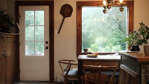 A kitchen with a wooden door, a window with a view of greenery, a hanging wooden paddle, and a chandelier. - Hudson Pond · Garden Queen Suite · GF Breakfast (Poughkeepsie)