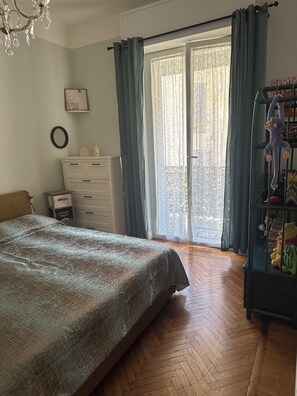 A bedroom with a bed, a dresser, a shelf with toys, a chandelier, and a window with curtains. - Bright apartment in the heart of San Remo (Sanremo)