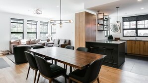 A modern kitchen with a central island, a dining area with a wooden table and chairs, and a seating area with a sofa and cushions. - Le Contemporain by Gestion ELITE (Mont-Tremblant)