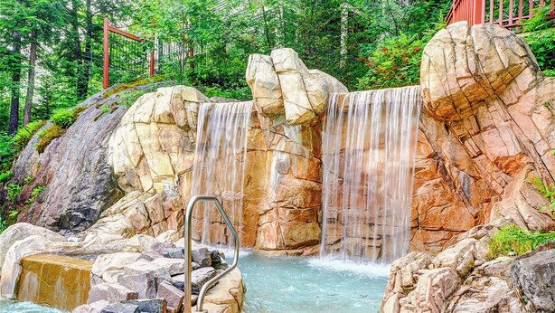 A natural rock formation with a waterfall and a metal ladder leading into a pool. - Le Contemporain by Gestion ELITE (Mont-Tremblant)