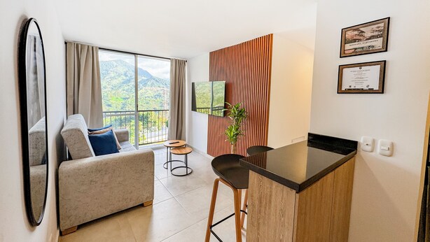 A modern room with a sofa, a small table, a TV, and a balcony with a mountain view. - MonteAzul apto con vista a la Cordillera (Armenia)