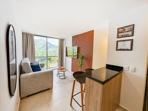 Una habitación moderna con sofá, una mesita, televisor y balcón con vistas a la montaña.