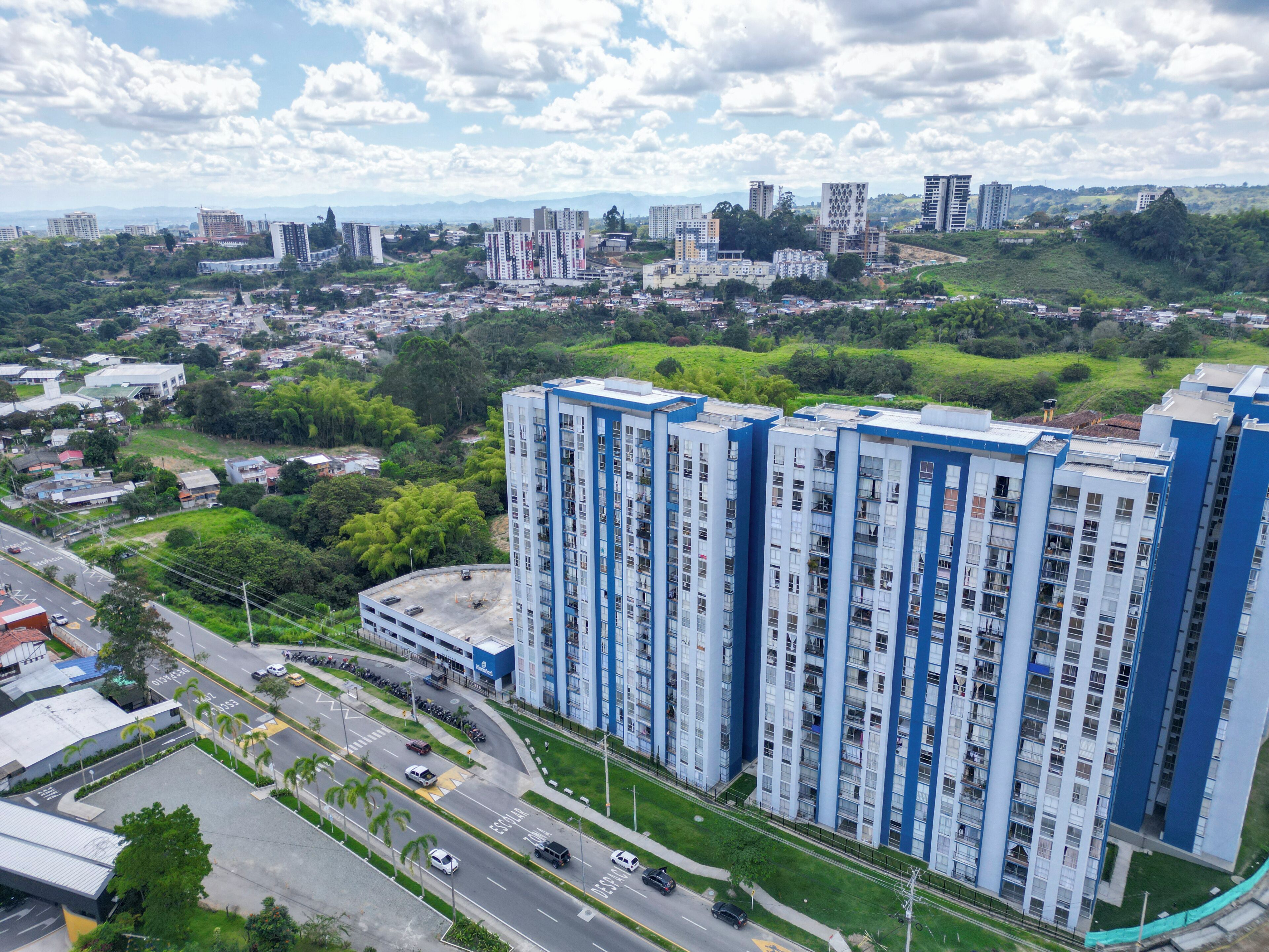 A high-rise building with multiple floors, surrounded by greenery and a road with vehicles.
