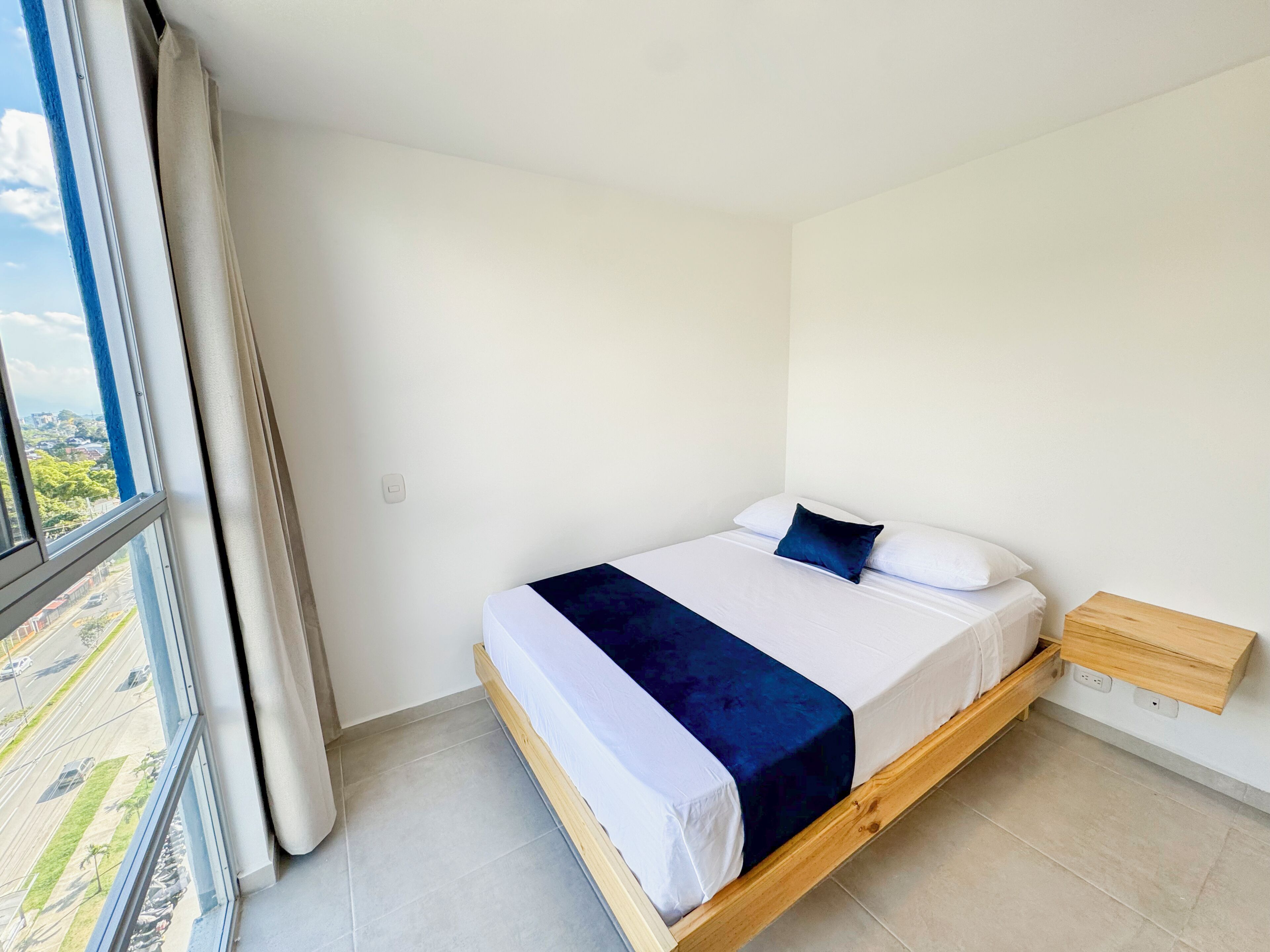 A single bed with a wooden frame, white bedding, and a dark blue accent pillow.
