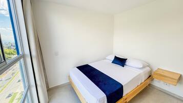 A single bed with a wooden frame, white bedding, and a dark blue accent pillow.