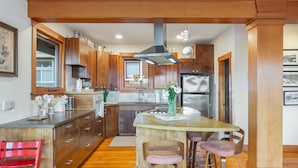 A modern kitchen with wooden cabinets, a stainless steel refrigerator, and a central island with bar stools. - Tatalias House ~ Near Space Needle~Sports Arena~Sea Center~AC~Parking~PetsOK~NFL (Seattle)