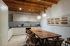 A kitchen with wooden ceiling beams, white cabinets, a dining table with chairs, and pendant lights. - Villa Qupi, sleeps 12, Fully Air-conditioned, stunning views of the Acropolis! (Lindos)