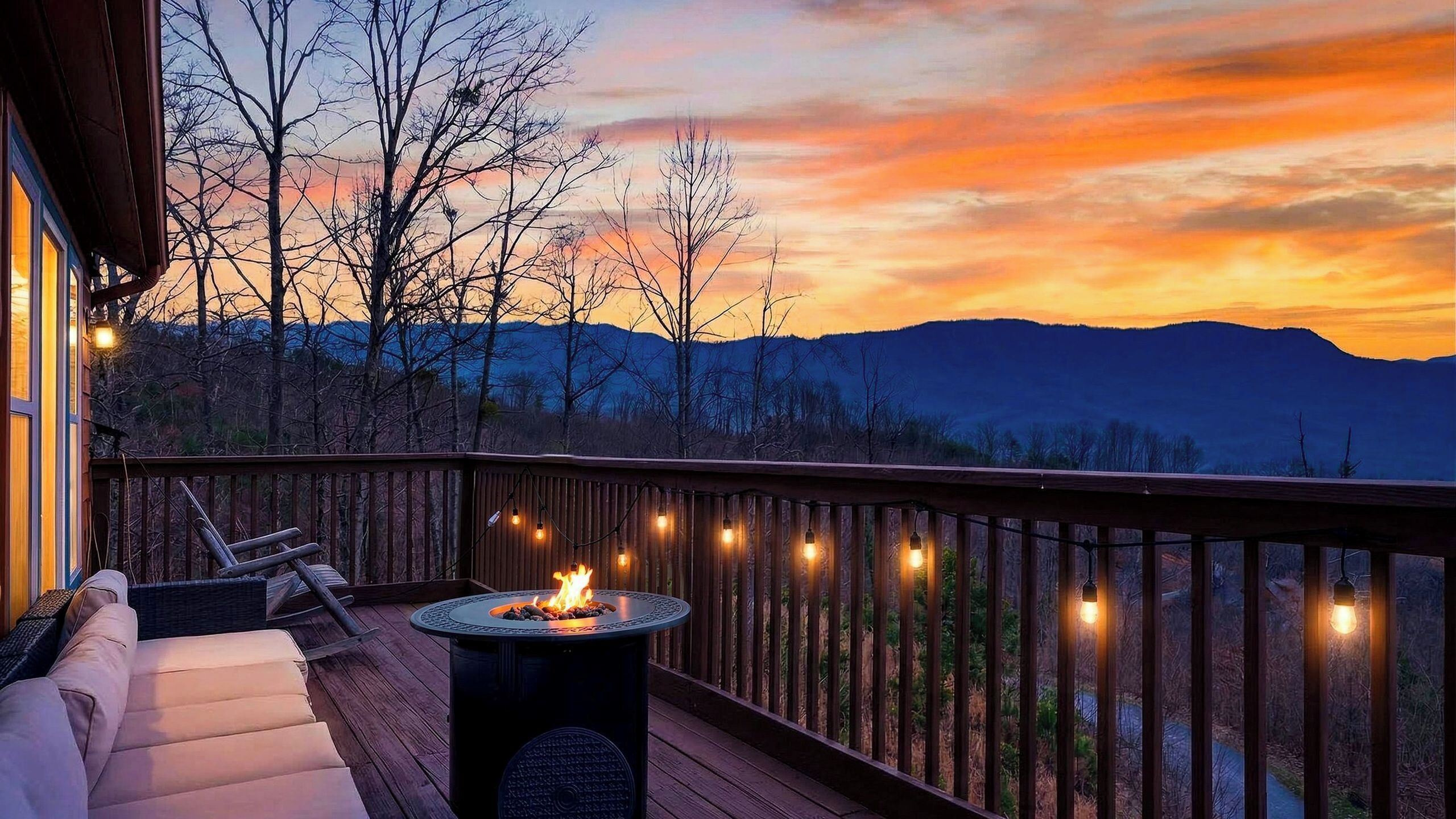 A deck with a fire pit, outdoor seating, and string lights against a sunset backdrop.