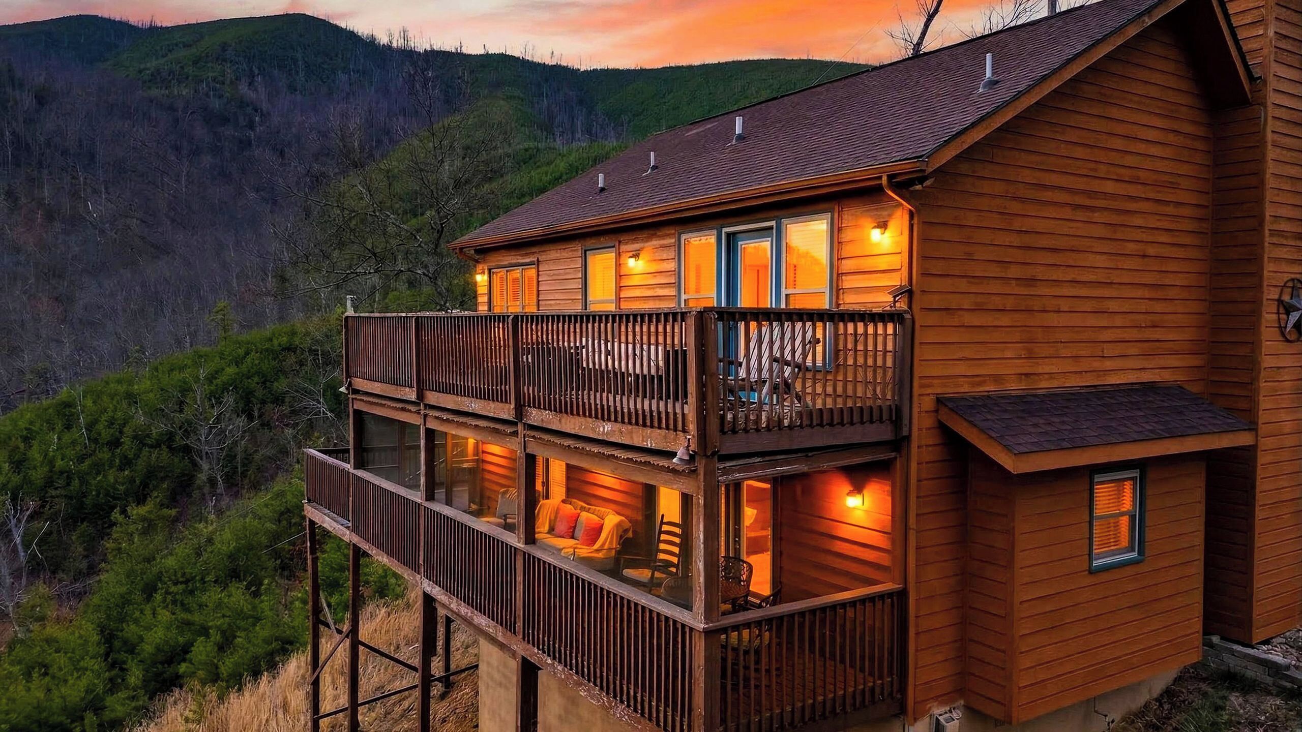 A wooden cabin with a balcony, multiple windows, and a view of the surrounding forest.