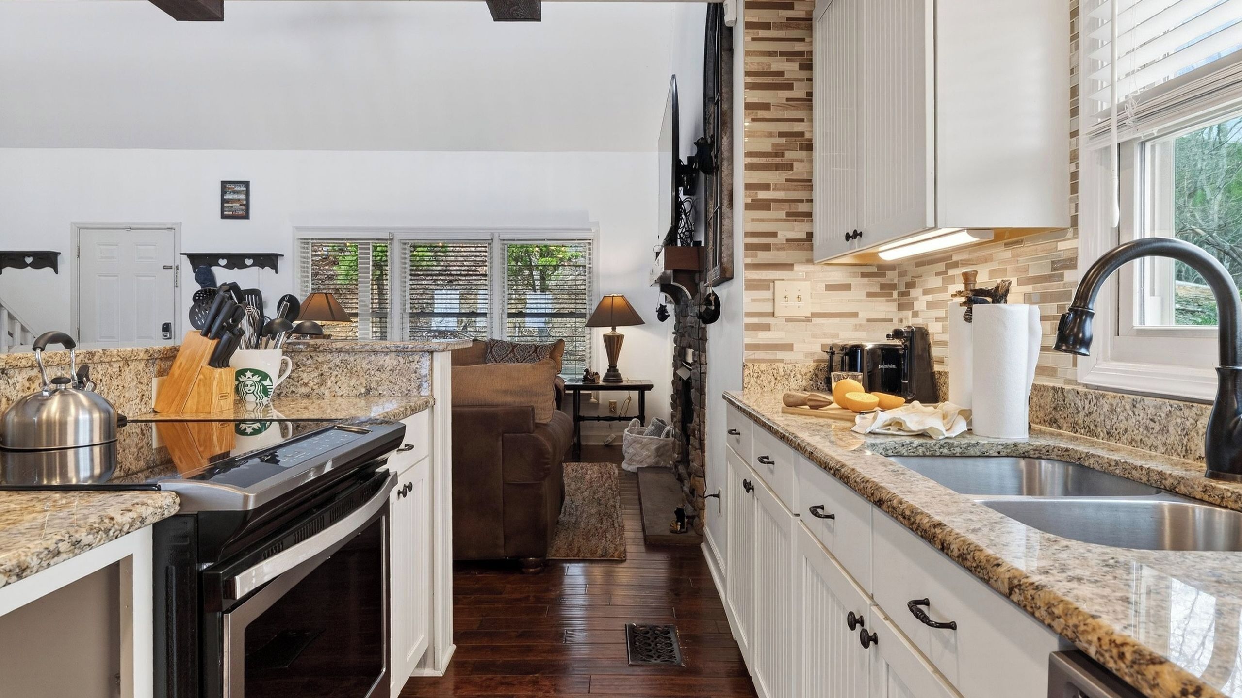 A kitchen with granite countertops, a stove, a sink, and a dining area with a couch.