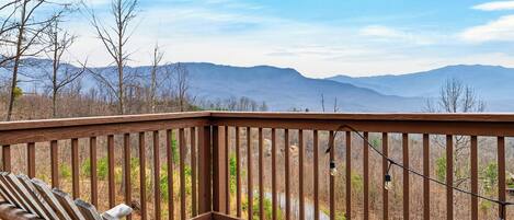 A wooden deck with a bench, overlooking a mountainous landscape.