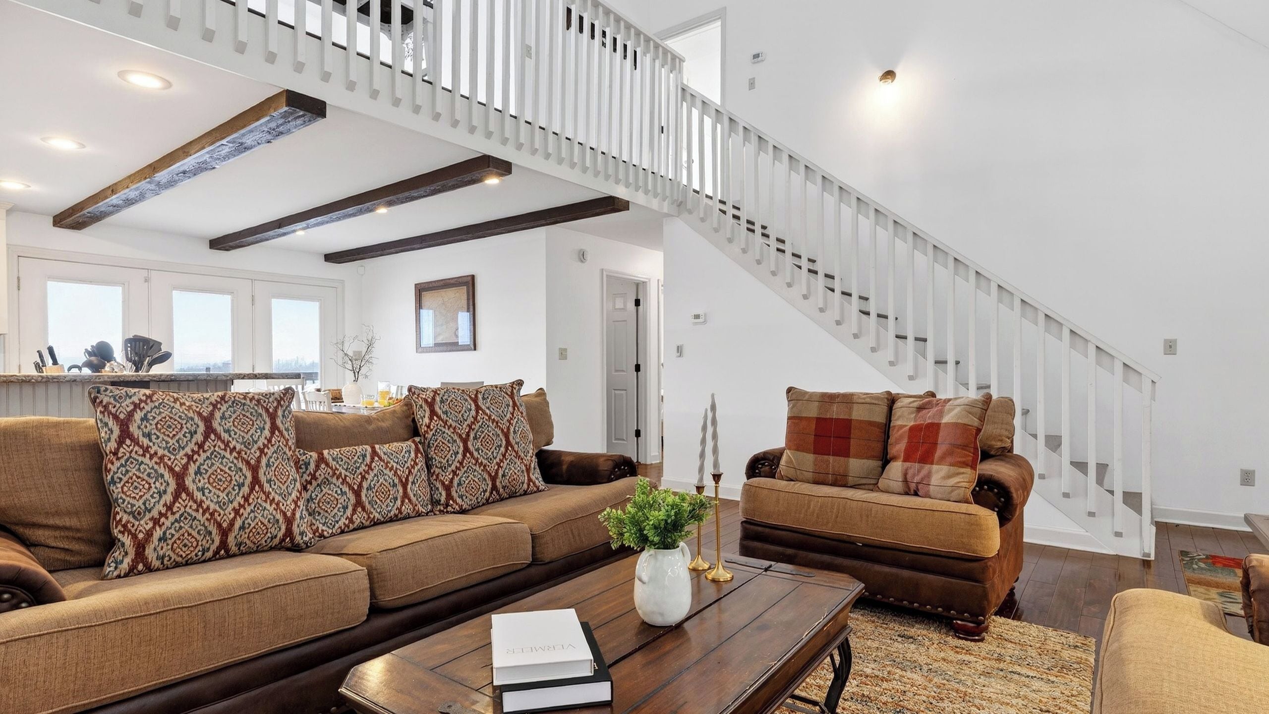 A spacious living room with a high ceiling, a staircase, and a kitchen in the background.