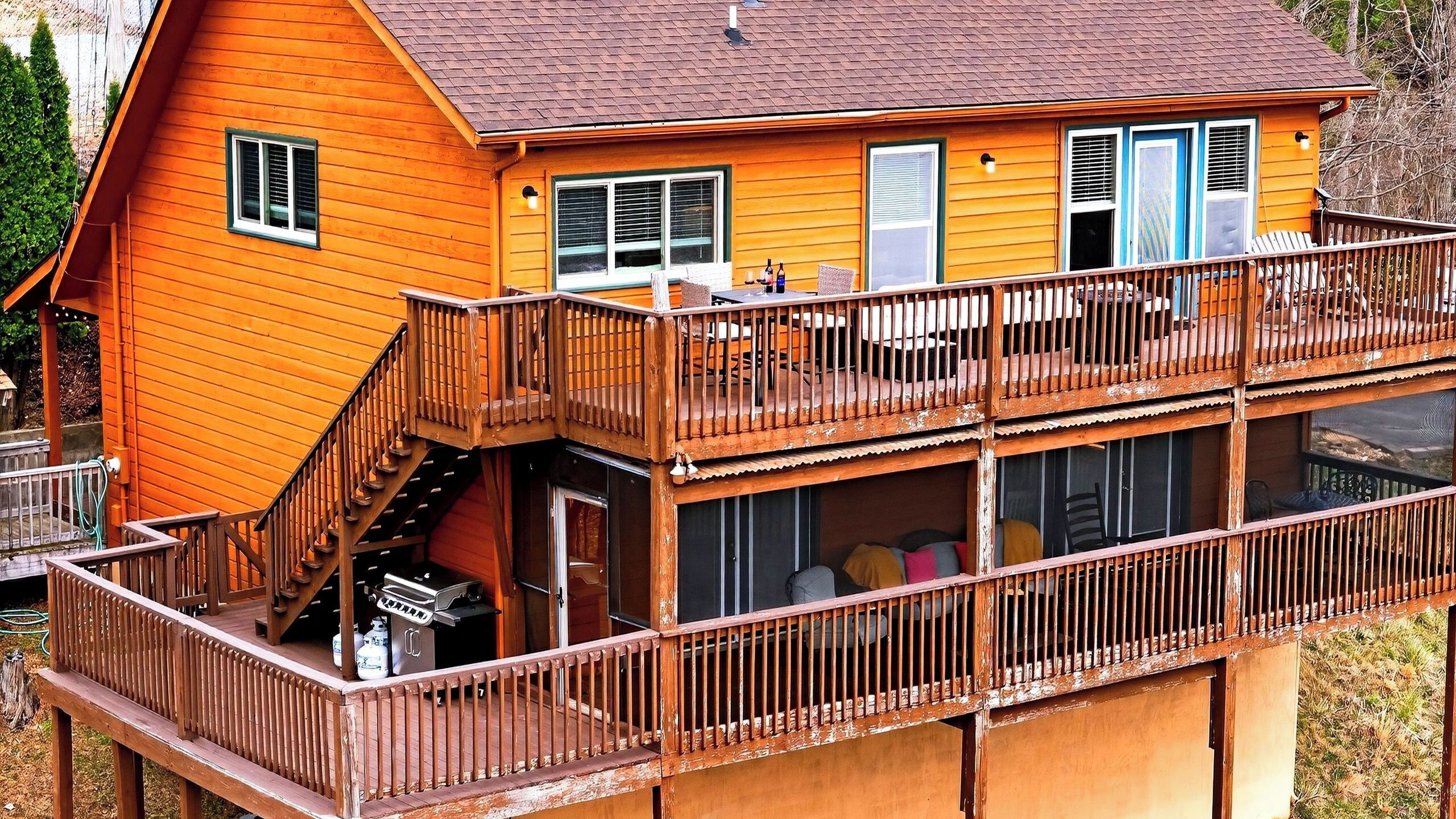 A multi-level wooden house with a balcony, a staircase, and a barbecue area.