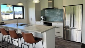 Et moderne køkken med en central ø, rustfrie hvidevarer og hængende lamper.