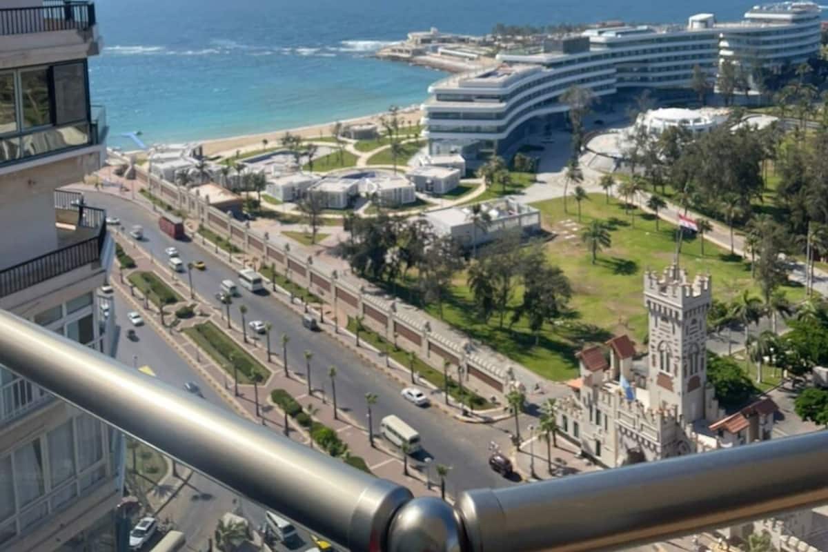 A coastal cityscape with modern buildings, a beach, and a historic tower.