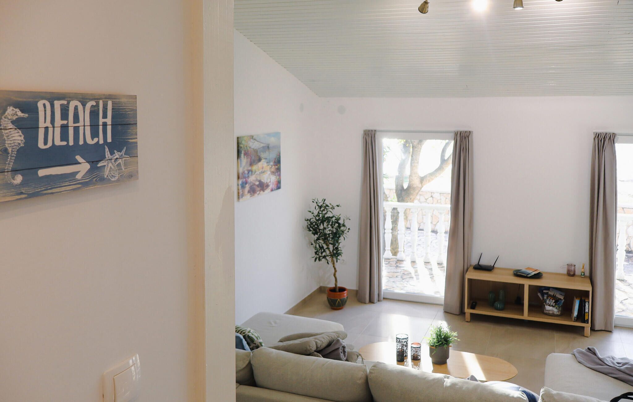A living room with a sofa, a coffee table, a potted plant, a bookshelf, and a painting on the wall.