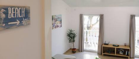 A living room with a sofa, a coffee table, a potted plant, a bookshelf, and a painting on the wall.