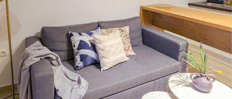 A grey sofa with patterned cushions, a small round table with a teapot, and a floor lamp.