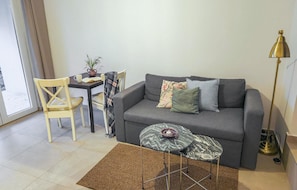 A living room with a grey sofa, a small round table, a floor lamp, a chair, and a dining table with a vase and book. - Lovely apartment in Krusevo with WiFi (Krusevo)
