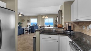A modern kitchen with a dining area, a view of the ocean, and a ceiling fan. - Stunning corner unit in the heart of Pensacola beach with panoramic views. (Pensacola Beach)