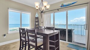 A dining area with a view of the ocean, a chandelier, and a sign indicating a 5 o'clock somewhere. - Stunning corner unit in the heart of Pensacola beach with panoramic views. (Pensacola Beach)