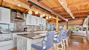 Una cocina moderna con encimeras de mármol, vigas de madera e iluminación colgante.