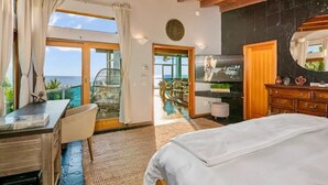 Un dormitorio con cama, escritorio, silla, espejo grande y vista al océano.