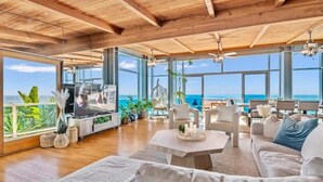 Un espacio habitable amplio con techo de madera, ventanas grandes que ofrecen vistas al océano y muebles modernos.