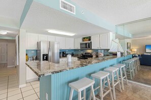 A kitchen with white cabinets, a granite countertop, and a blue accent wall. - Spacious gulf front condo with beach access and seasonal beach service (Okaloosa Island)