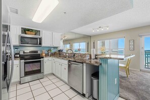 Una cocina moderna con electrodomésticos de acero inoxidable, lavavajillas y un amplio ventanal con vistas a un balcón.