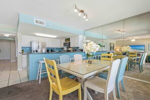 A modern kitchen with white cabinets, a blue island, and a dining area with a glass table and chairs. - Spacious gulf front condo with beach access and seasonal beach service (Okaloosa Island)
