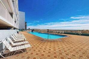 A rooftop pool with lounge chairs, a clear blue sky, and a modern building in the background. - Spacious gulf front condo with beach access and seasonal beach service (Okaloosa Island)