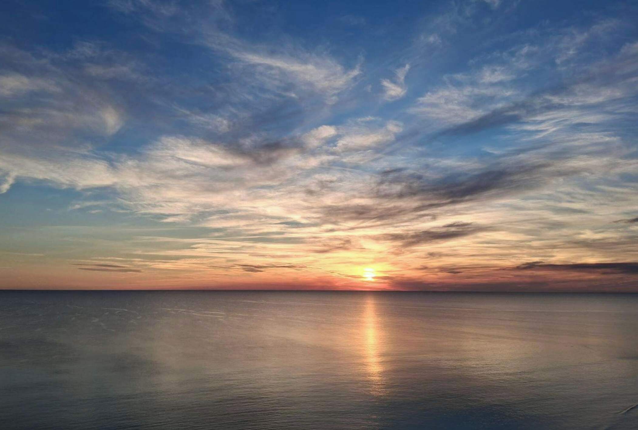Ein Sonnenuntergang über einem ruhigen Meer mit klarem Horizont.