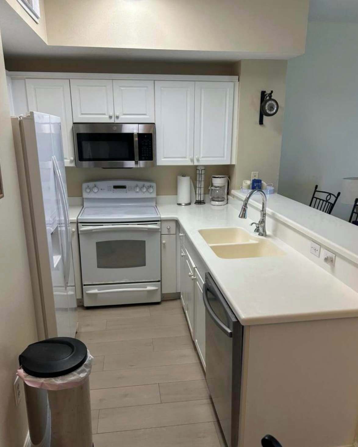 Cocina compacta con armarios blancos, microondas de acero inoxidable, horno empotrado, lavavajillas y un lavabo.