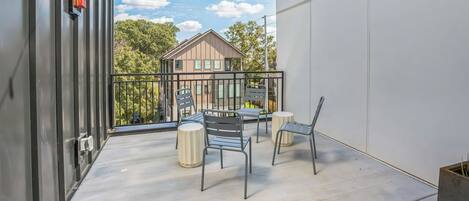A balcony with a table and chairs, a fire alarm, and a view of a building with trees.