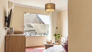 Ett hotellrum med en säng, ett skrivbord, ett fönster med utsikt över ett berg och en hängande lampa.