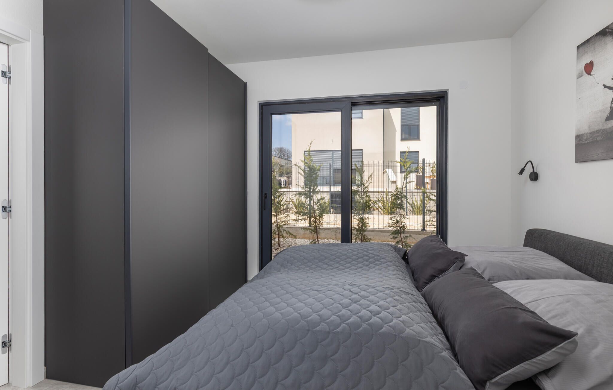 Una camera da letto moderna con un letto, un armadio e un'ampia finestra vista edifici e alberi.