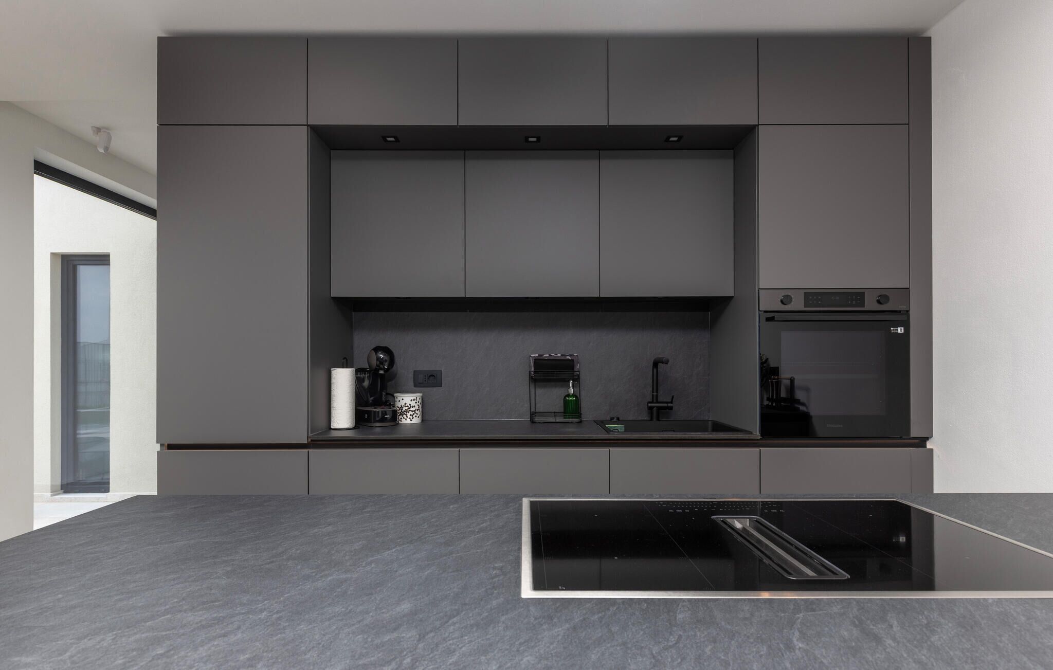 Una cocina moderna con horno integrado, cafetera y una encimera negra elegante.