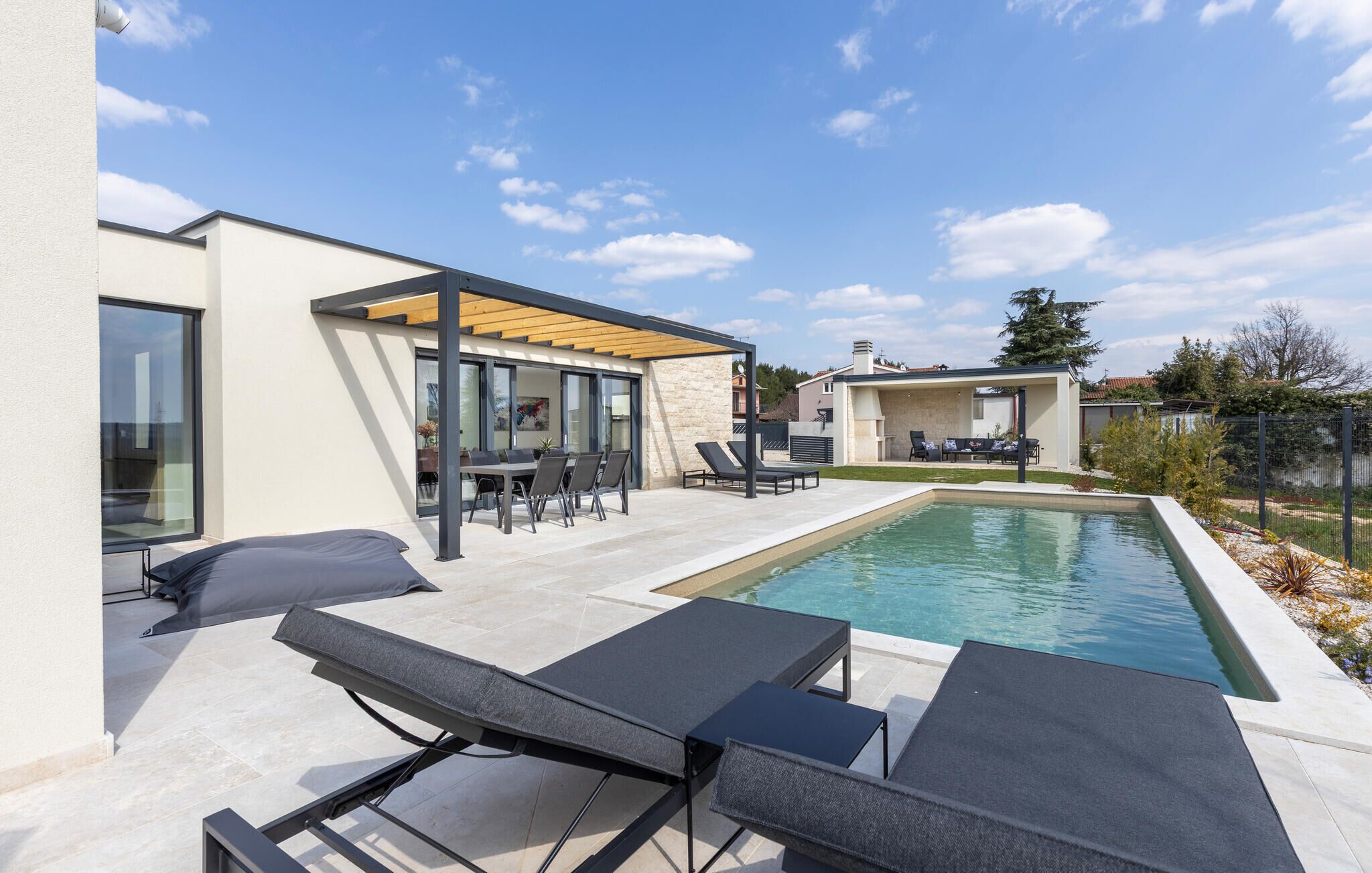 Un espace piscine extérieur moderne, doté de chaises longues, d’un coin salon abrité et d’un mur en pierre.