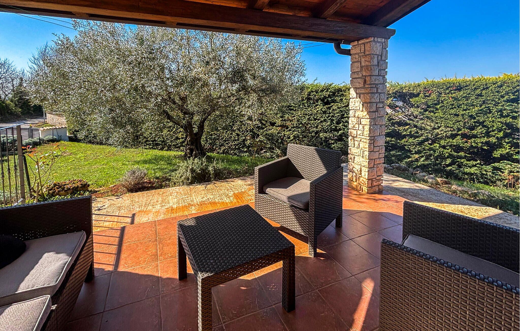 An outdoor patio with wicker furniture, a stone pillar, and a view of a lush garden.