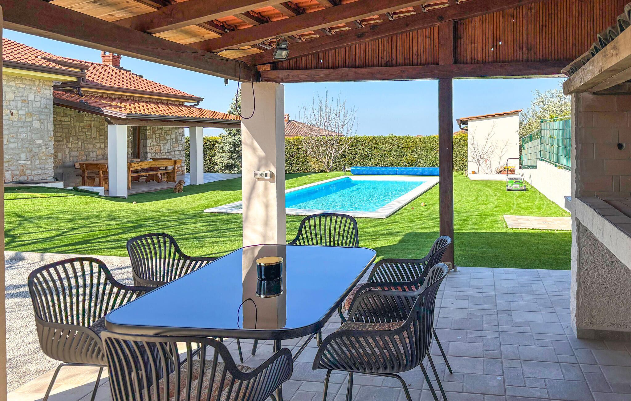 Une terrasse couverte avec une piscine, des sièges d’extérieur et un bâtiment en pierre en arrière-plan.