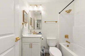 A bathroom with a toilet, sink, mirror, and bathtub.