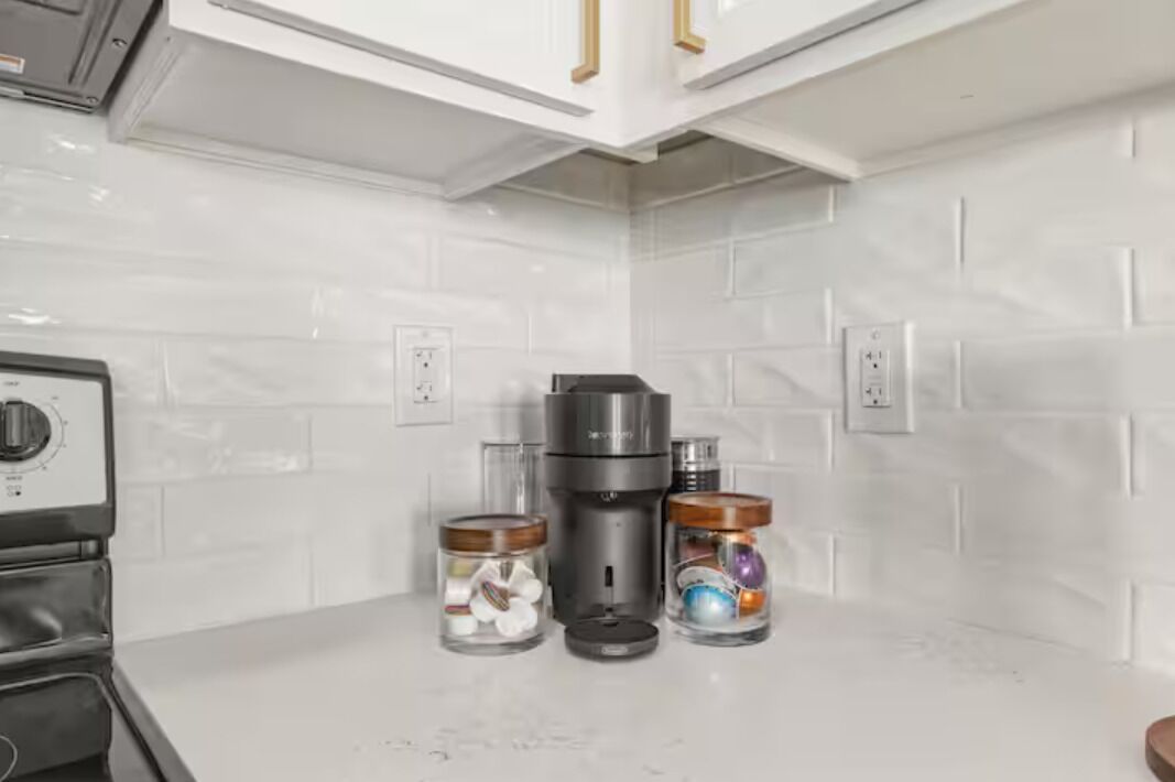A kitchen with white tiled walls, a coffee maker, and two glass jars with lids.