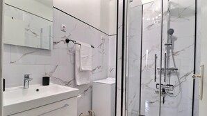 Een moderne badkamer met een glazen douchecabine, een wastafel met spiegel en een handdoekhouder.