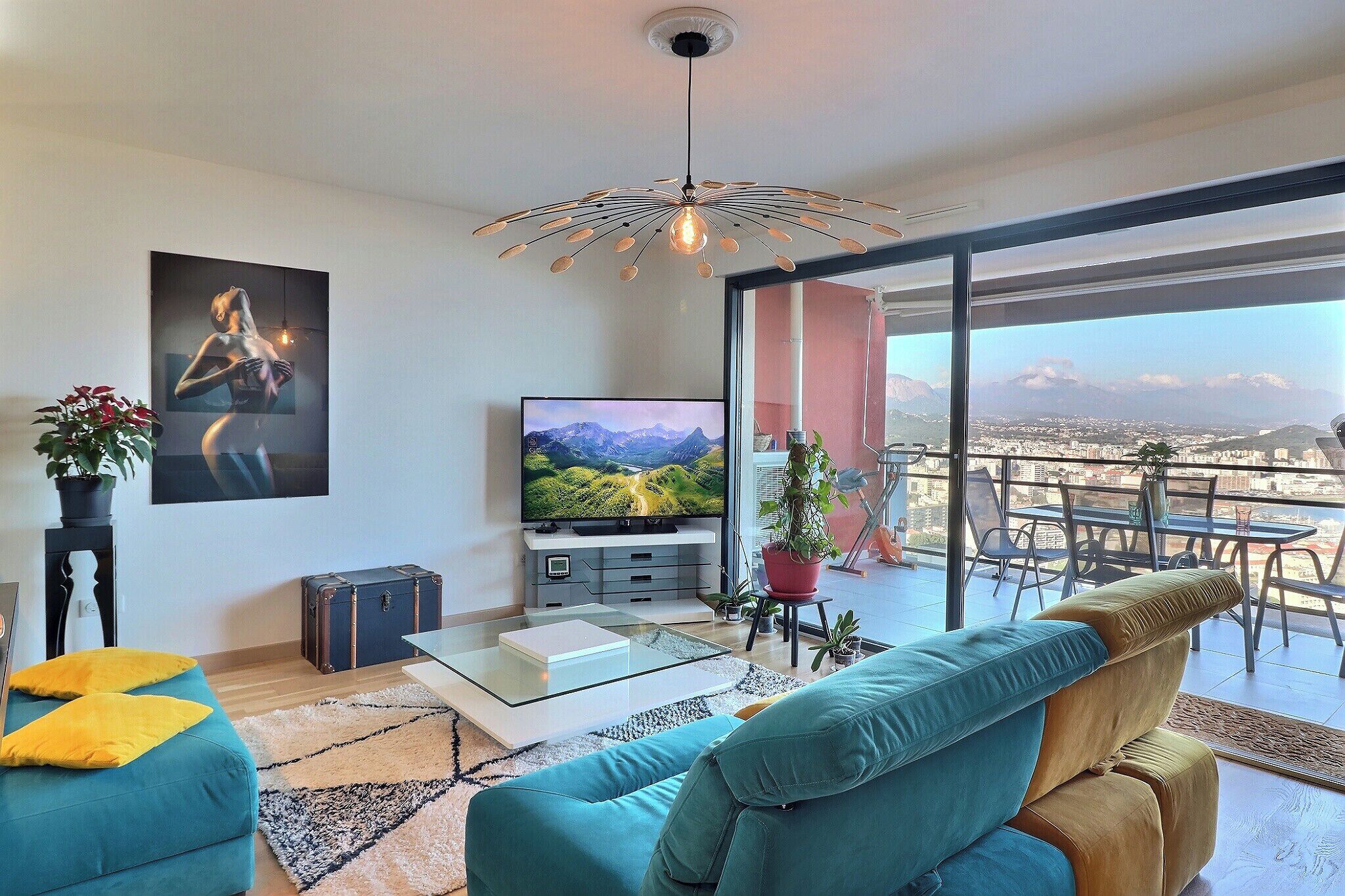 Una sala de estar moderna con televisor, sofá y un balcón con vistas a la ciudad.