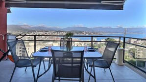 Een balkon met een tafel, stoelen, een bloempot en uitzicht op een stadsbeeld en bergen.
