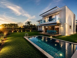 Uma casa moderna de dois andares, com piscina, área de estar externa e um jardim bem cuidado.